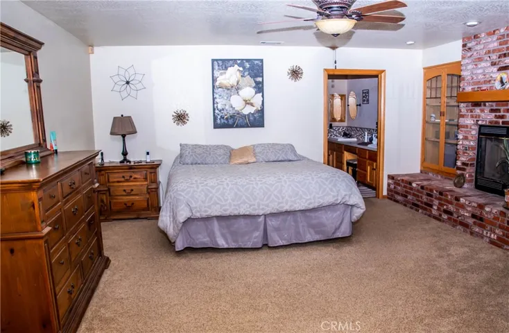 Giant Primary bedroom with brick faced fireplace, ceiling fan, and double door access to the rear patio.
