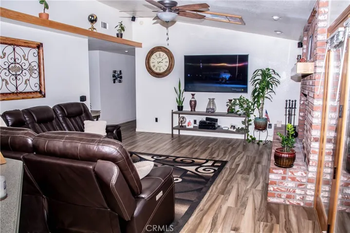 Living room with wood grain tile floors, vaulted ceiling, ceiling fan, and brick faced fireplace