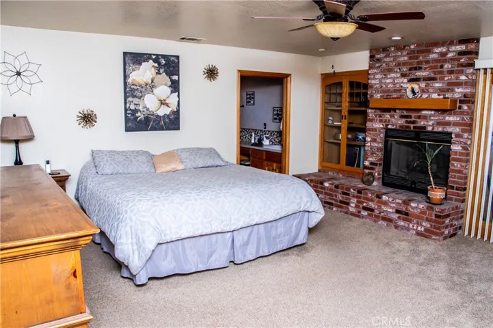 Giant Primary bedroom with brick faced fireplace, ceiling fan, and double door access to the rear patio.