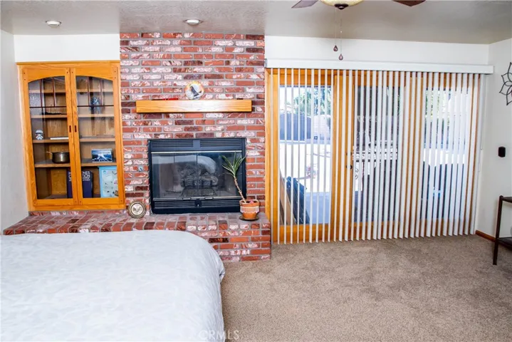 Giant Primary bedroom with brick faced fireplace, ceiling fan, and double door access to the rear patio.