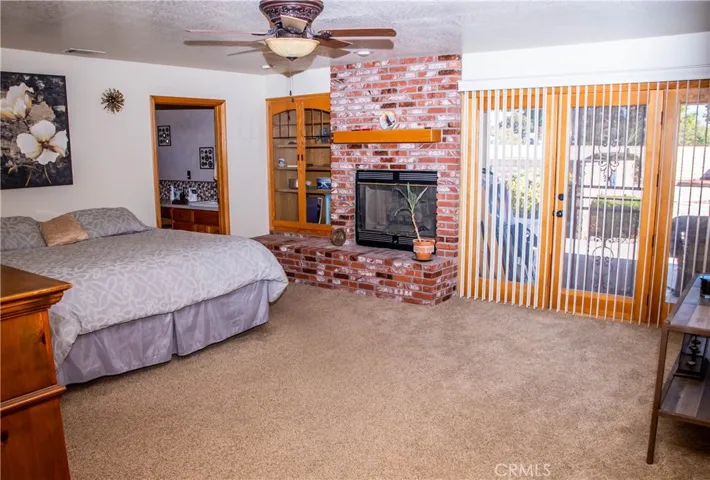 Giant Primary bedroom with brick faced fireplace, ceiling fan, and double door access to the rear patio.