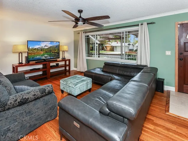The living room is bathed in natural light from a large picture window and is further enhanced by crown molding, a designer lighted ceiling fan and gleaming hardwood floors.