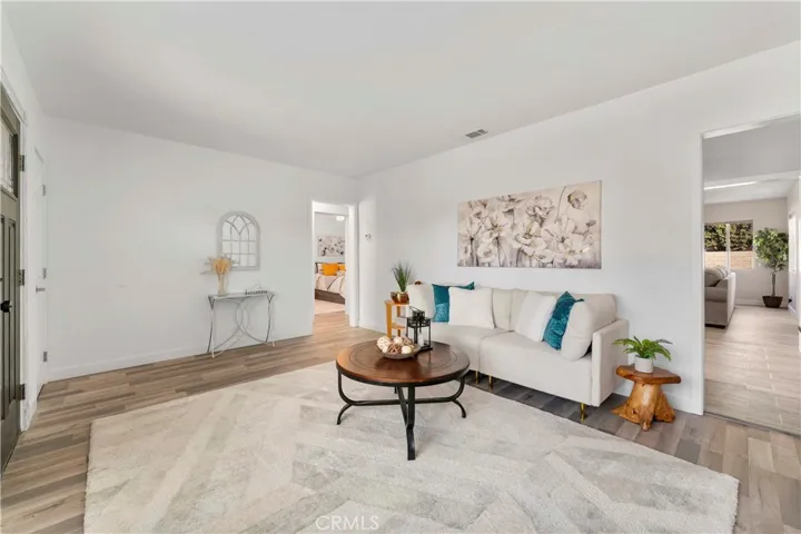 Formal living lovingly updated with luxury vinyl plank flooring and double pane windows and door/screen door and paint. Left of image is small hallway to the bedrooms and one of the bathrooms. Throughway on the right leads to open space kitchen/family/dining/laundry/second bath.