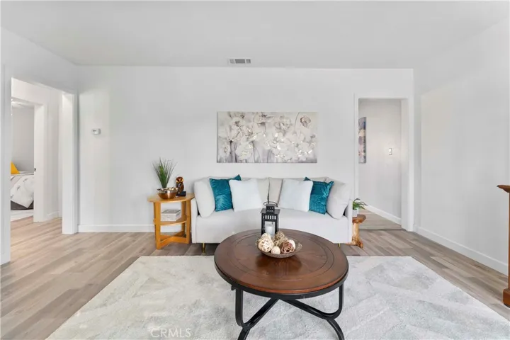Formal living lovingly updated with luxury vinyl plank flooring and double pane windows and door/screen door and paint. Left of image is small hallway to the bedrooms and one of the bathrooms. Throughway on the right leads to open space kitchen/family/dining/laundry/second bath.