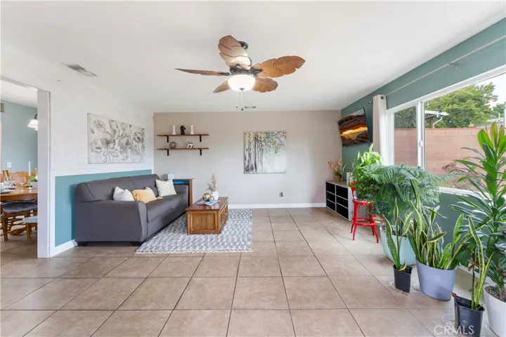 Super spacious family room with tile flooring and large picture window of the backyard and ceiling fan with palm leave designed blades. If desired for more open space to dining and kitchen, then the wall behind the couch could be removed. Current owners put it up to have separate living area.