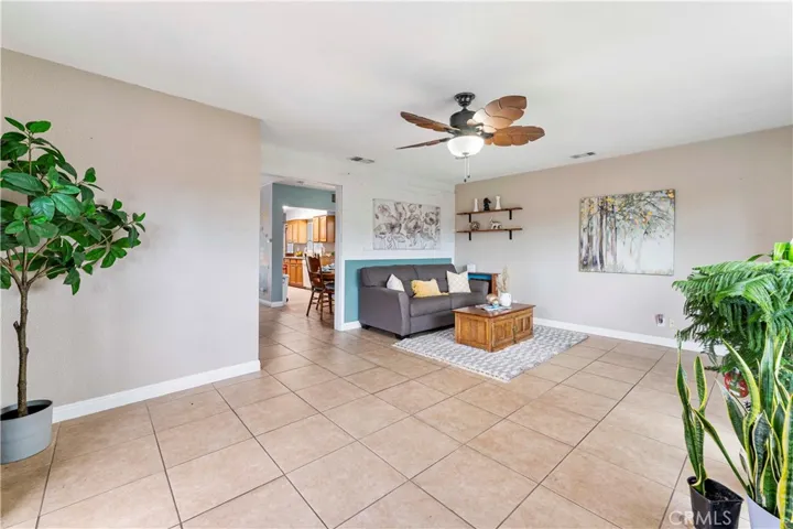 Super spacious family room with tile flooring  and ceiling fan with palm leave designed blades. If desired for more open space to dining and kitchen, then the wall behind the couch could be removed. Current owners put it up to have separate living area.