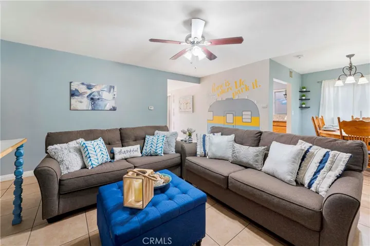 Living room with tile flooring and ceiling fan. Right of image is the dining area right off from the galley kitchen. The entry is the throughway in the middle of the picture. Left of image is the hallway to the bedrooms and bathrooms.