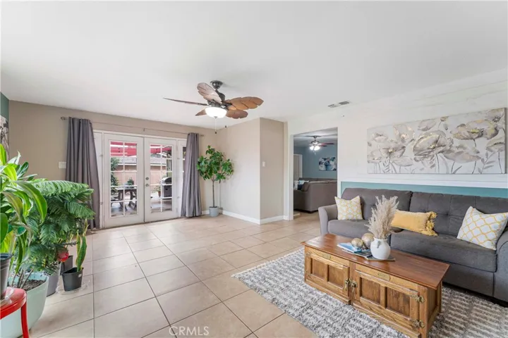 Super spacious family room with tile flooring and large picture window of the backyard and ceiling fan with palm leave designed blades. If desired for more open space to dining and kitchen, then the wall behind the couch could be removed. Current owners put it up to have separate living area.  French doors to concrete patio and spacious backyard.