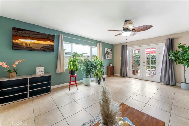 Super spacious family room with tile flooring and large picture window of the backyard and ceiling fan with palm leave designed blades. French doors to concrete patio and spacious backyard.