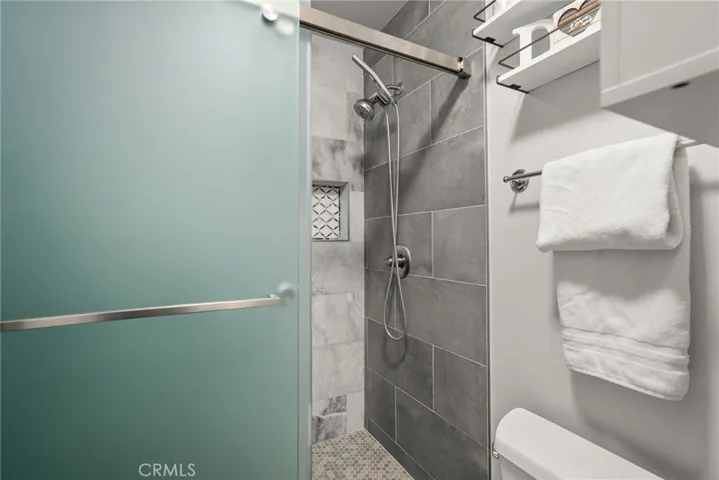 Primary walk-in shower with glass sliding door and hand-held shower faucet.