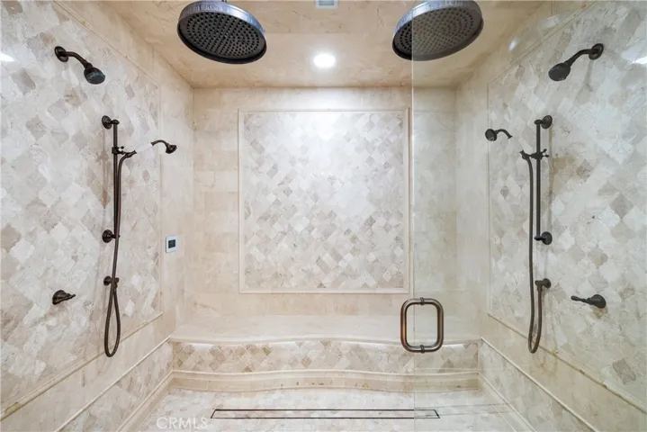 Primary walk-in steam shower with custom under seat lighting, six shower heads, full glass enclosure doors.