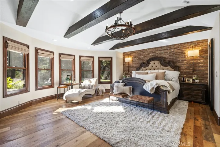 Primary main floor bedroom completely remodeled with 100 year old barn wood floors, a brick accent wall, beamed ceilings, automatic shades, custom lighting, and built-in cabinetry with drawers.