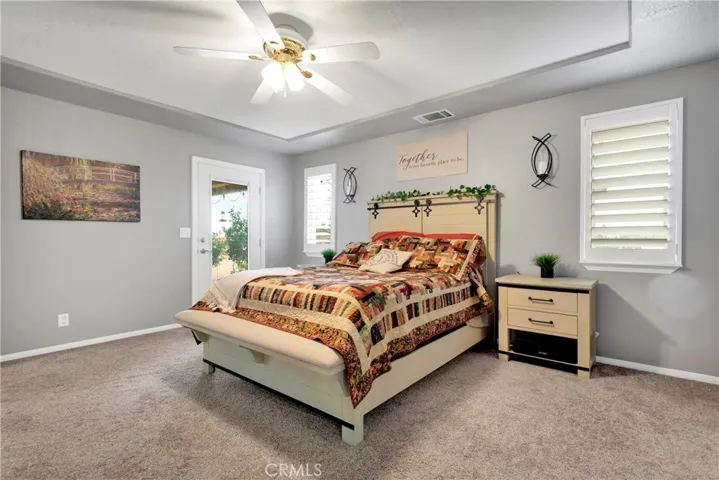 Primary suite with hand textured ceilings, plantation shutters, French door to large covered patio, tray ceiling in two tone paint.