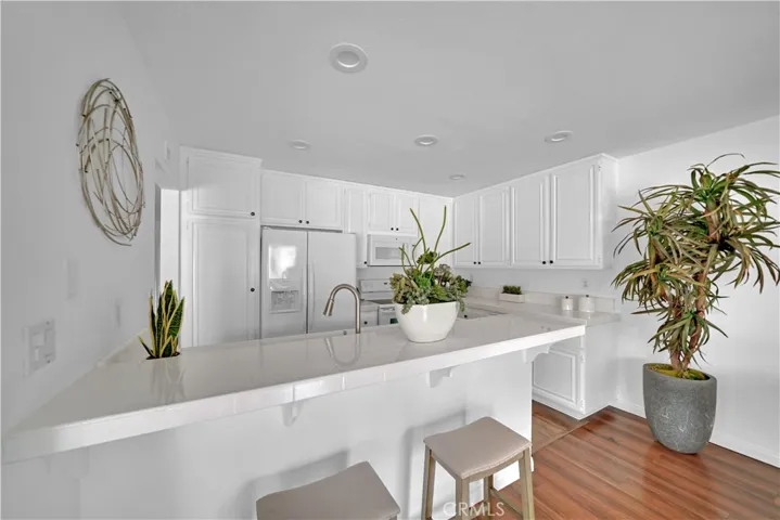 Bright Kitchen with Recessed LED Lighting, White Tile Countertops, Breakfast Bar, and White Shaker Cabinetry