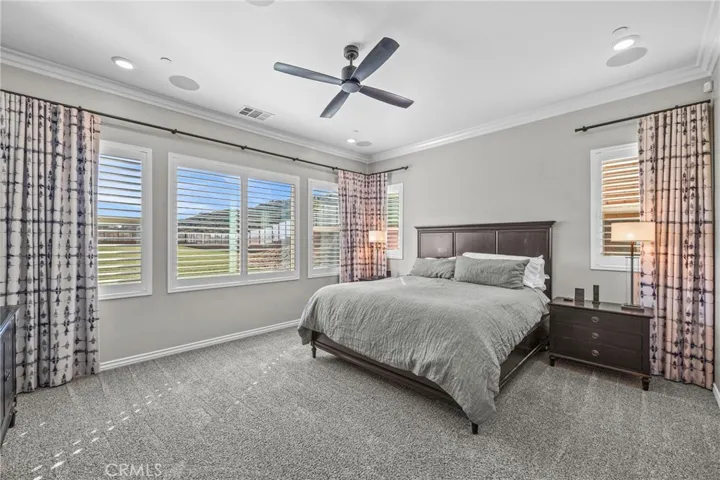 Spacious primary bedroom freshly painted, newer carpet, custom shutters, custom window coverings, surround sound, ceiling fan, and crown molding