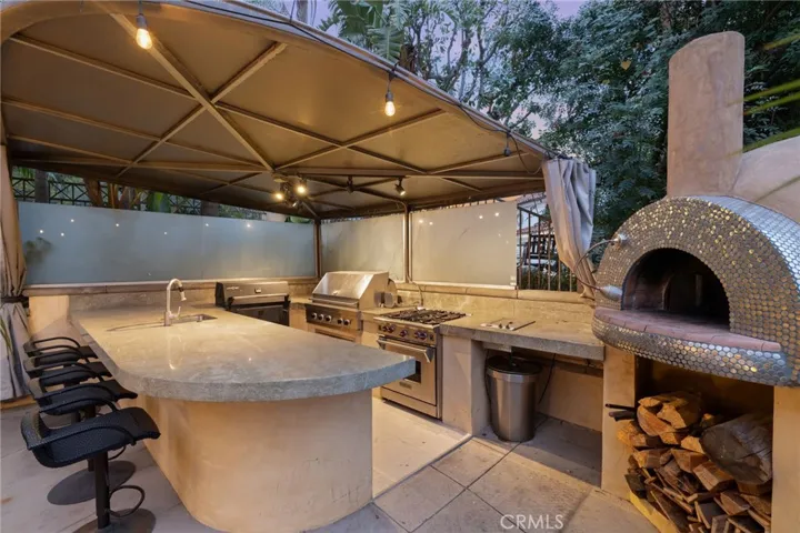 Partially covered outdoor kitchen with wood burning pizza oven, three grills (two gas, one charcoal), a deep fryer, and a sink. Plus barstool seating. Perfect party setup.