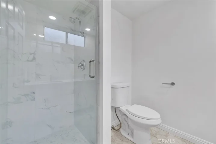 Newly remodeled shower with new marble tiles, shower fixture, glass door and new toilet