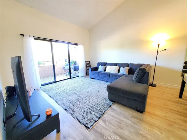 Living room features laminated flooring, vaulted ceiling and glass sliding doors leading out to a large balcony with treetop and park view.