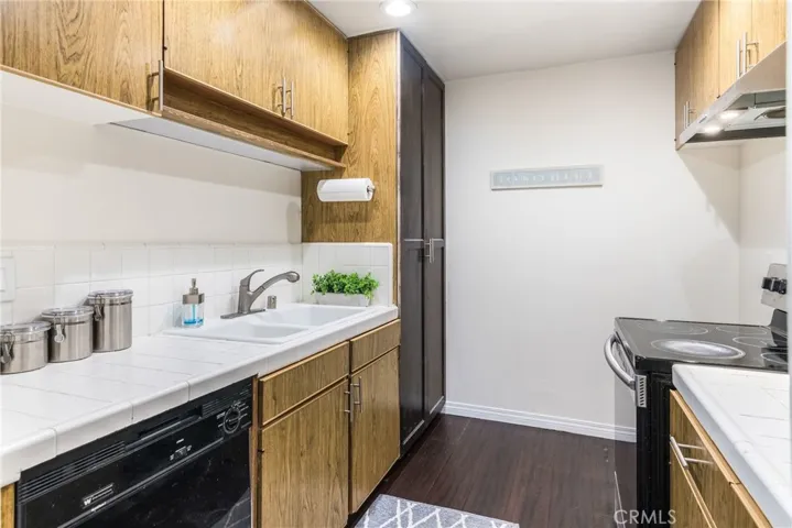 Kitchen with dark hardwood floors, while tile counters, and laminate wood cabinetry
