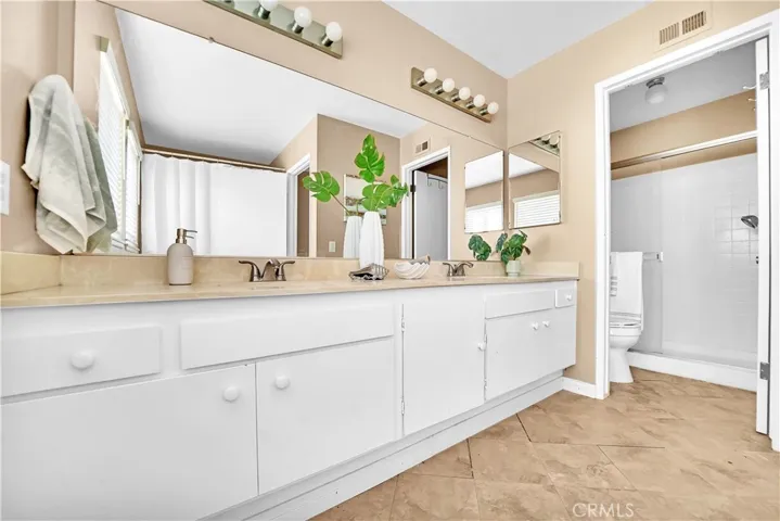 The large guest bathroom includes dual sinks, a privacy toilet area, a walk-in shower with a glass door, and a separate soaking tub (not shown)