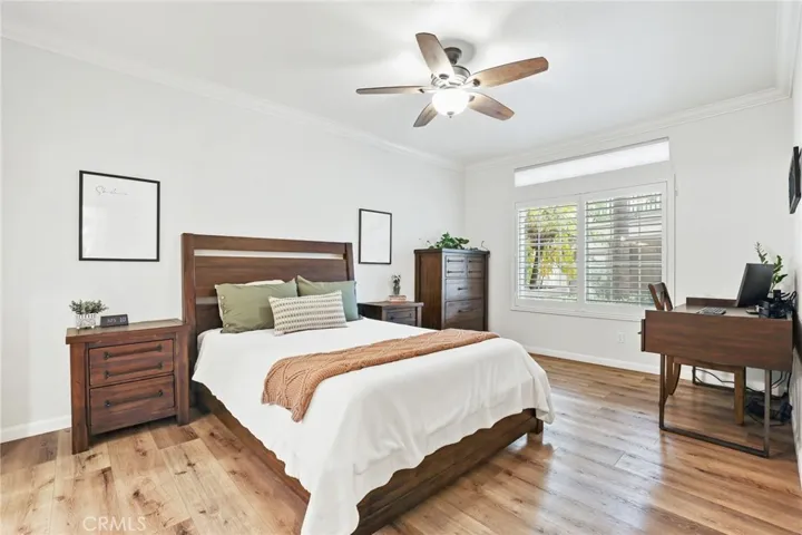 The spacious master bedroom features a vinyl plank floor, ceiling fan with light, crown molding and plantation shutters.