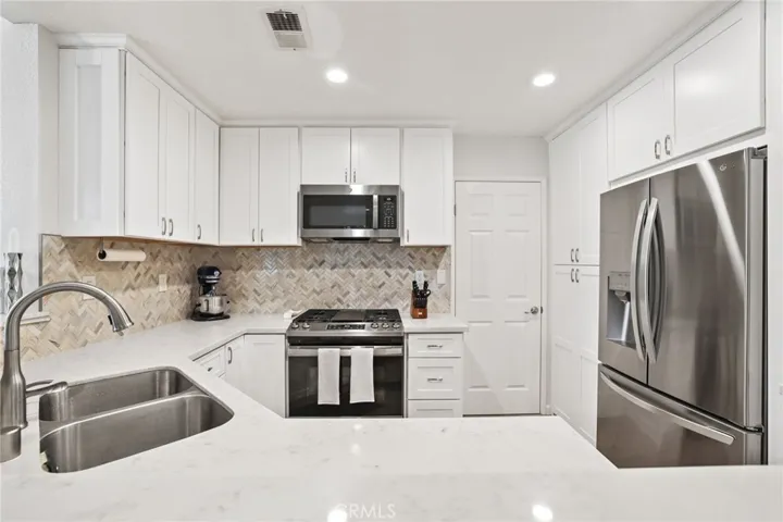 The remodeled kitchen features a quartz countertop, gleaming white cabinetry, herringbone design stone backsplash, double stainless steel sink with soap dispenser, stainless steel oven with gas cooktop and microwave, and pantry with pull out shelves.  The laundry room is behind the raised panel door.