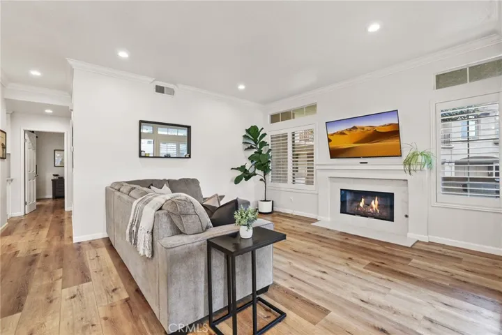 The living room features vinyl plank floor, crown molding, recessed lights, fireplace with quartz hearth, surround and covered mantle and plantation shutters.