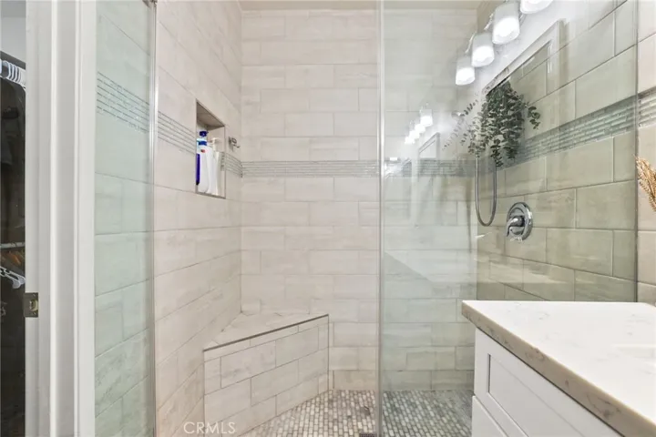 The custom tiled shower features a subway tiled floor, corner shower seat, recessed shampoo box, dual shower heads, decorative tiled glass band and frameless glass shower door.
