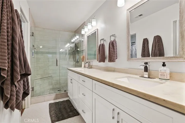 The remodeled master bath features a dual vanity with quartz counter and white cabinetry and lovely lighting above the dual mirrors and a tile floor.