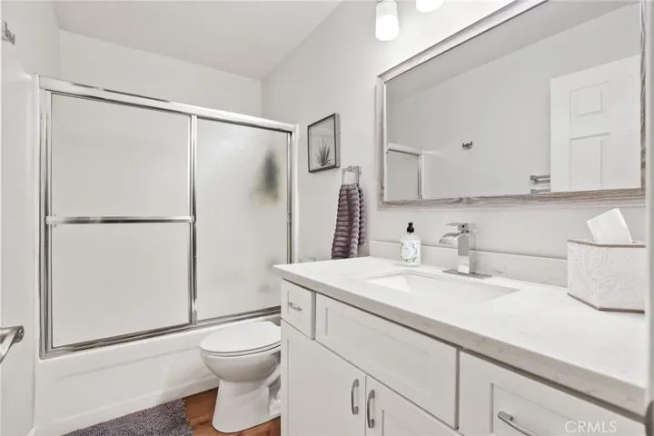 The updated secondary bath features a newer vanity with quartz counter and white cabinetry, newer lighting, toilet and mirror.