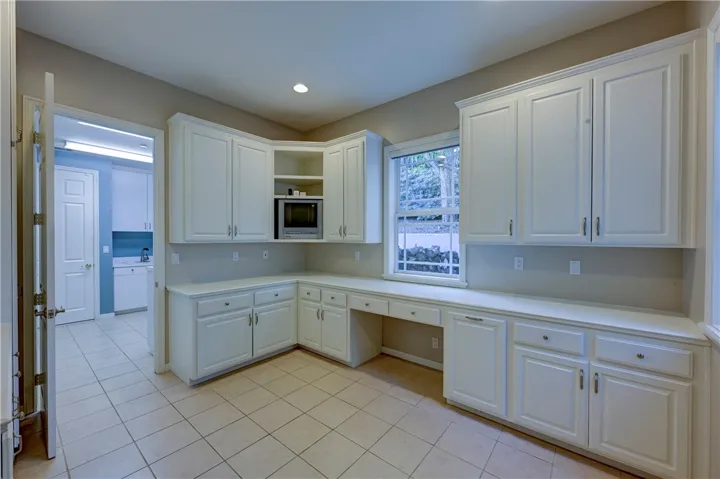 Spacious art / craft room with easy care flooring, a desk and window and lots of cabinetry.
