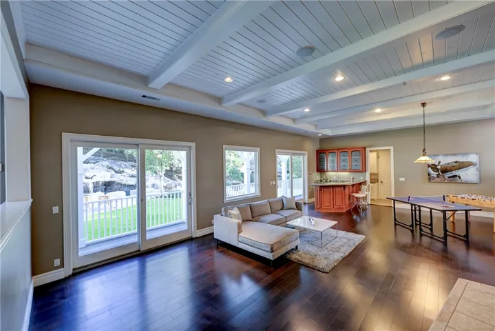 Family / Game room with beautiful beamed ceiling, a wet bar, a stone stacked floor to ceiling fireplace with hearth to the right of this photo and two sliders to the backyard make this the ultimate entertaining home.