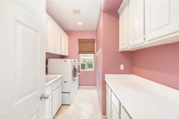 A cheerful laundry room painted in soft pink, equipped ample storage space, folding counter and sink