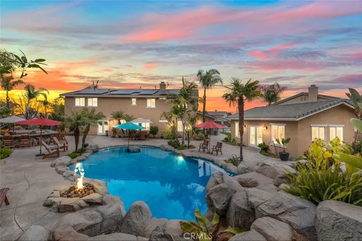 A backyard paradise revealed at dusk, featuring a sparkling pool, cozy fire pit, and ample space for entertaining under a canopy of palms.