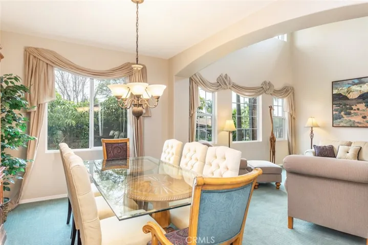 Elegant dining awaits in a room with a glass-top table and tufted chairs, framed by graceful curtains and garden views.