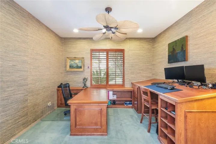 A stylish home office with textured walls, an executive desk, and tropical ceiling fan, ideal for productivity in comfort.