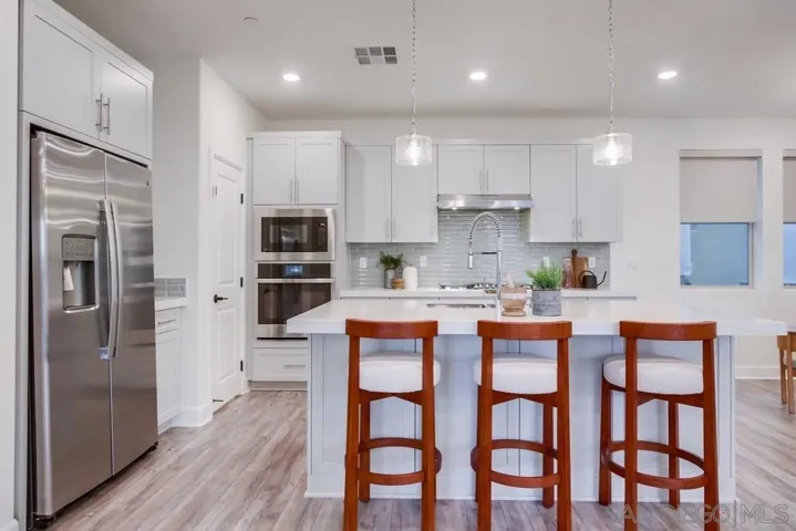 Tranquil biancone quartz counters with mitered edges, G.E. profile stainless steel appliances, Moen alighn high arc faucet, European soft-close drawers, glossy gray beveled tile backsplash, and more.