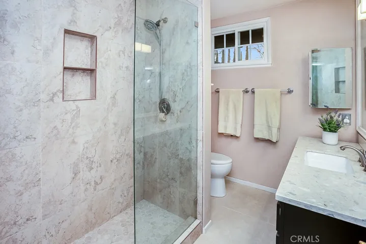 Remodeled guest bathroom (2020) that is enriched with a contemporary quartz crowned vanity with undermount basin, oversized framed dressing mirror, designer lighting, frameless glass-enclosed custom tiled step-in shower, dual flush commode and custom tiled floors.