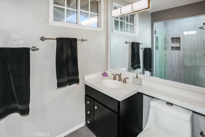 Private en suite remodeled (2012) primary bathroom with modern quartz crowned vanity, undermount basin, oversized framed dressing mirror, designer lighting, frameless glass enclosed custom tiled step-in shower with Solatube, single dual commode, and custom tiled floors.