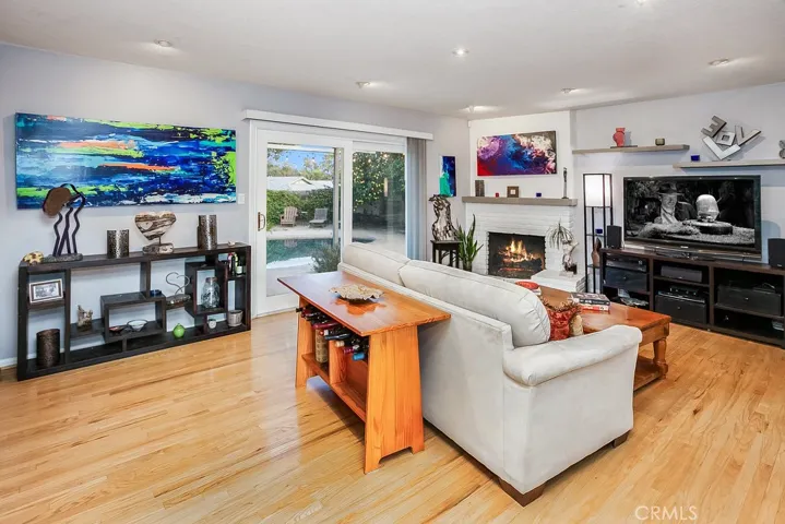 The family room that is bathed in natural light and is enhanced by recessed adjustable lighting, floating concrete shelving, a white brick fireplace with crushed glass, concrete mantle, rich oak hardwood floors and sliding glass doors that lead to the backyard.