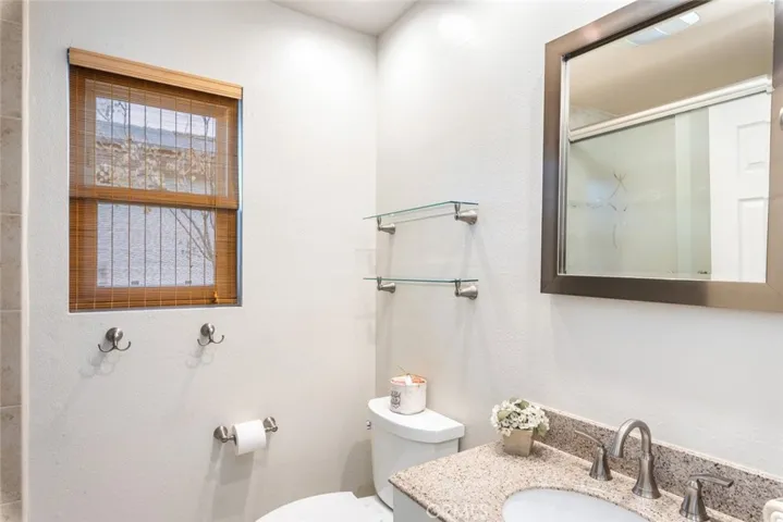 This bathroom boasts a clean and simple design, with a granite countertop sink complemented by modern fixtures. Natural light filters through the wooden blinds, offering both function and style in a compact space.