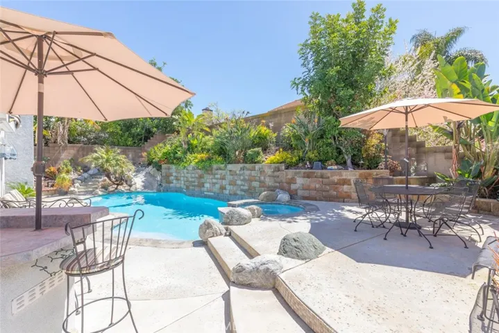 
An oasis-like backyard with a sparkling pool, cascading waterfall, and shaded seating areas nestled among vibrant greenery.