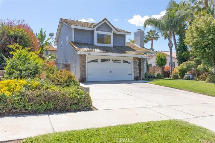 A charming two-story home with a stone facade, nestled in a vibrant garden.