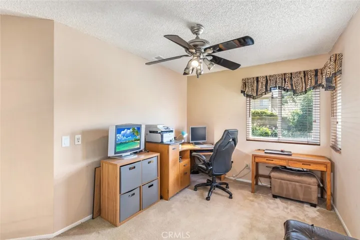 
Discover a compact and functional home office, bathed in natural light, poised for productivity. A ceiling fan above ensures a cool and breezy work environment.