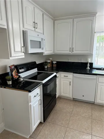 Kitchen with tile flooring, black counter tops and white cabinets