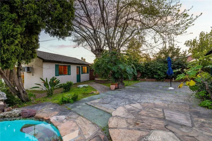 Backyard with a pool, flagstone decking, two outbuildings, pathways, and mature landscaping.