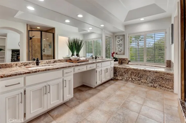 The primary bath features a dual vanity w/granite countertop, a soaking tub with a granite skirt, a separate walk-in shower w/travertine surround, a private water closet, & large walk-in wardrobe closet.