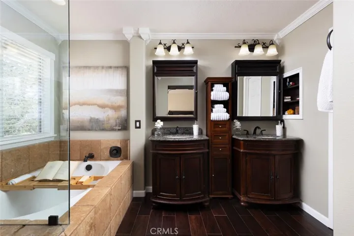 Master bath has wood look tile floors, dual vanities with cabinets and a walk-in closet.