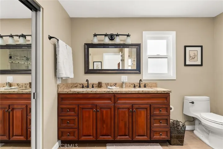 Primary bathroom with granite, double sinks, window and tile flooring.