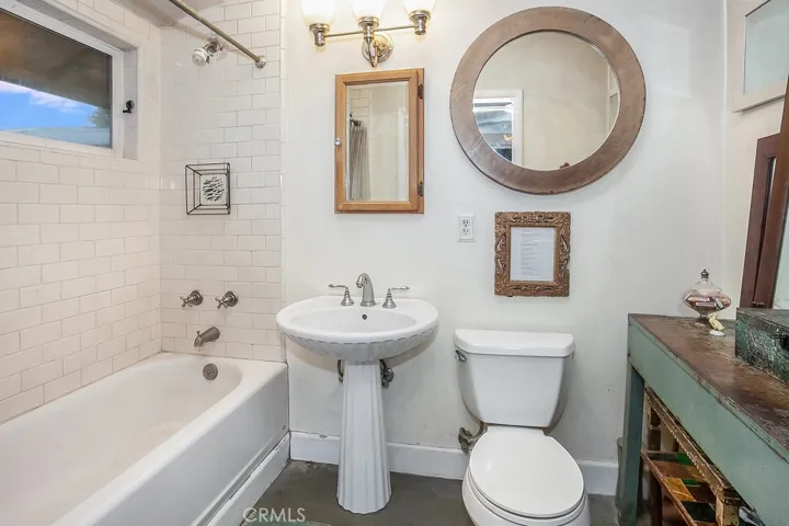 Ensuite primary bathroom with pedestal sink, subway tiled tub/shower with built-in niche for sundries and privacy window.
